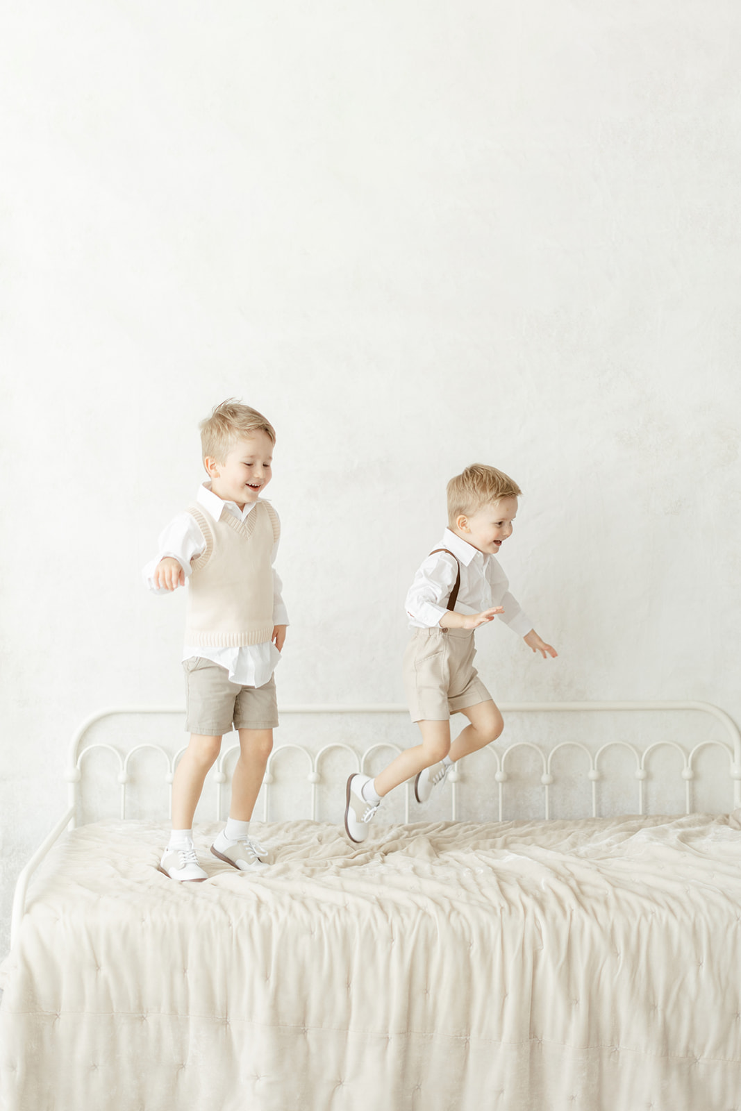Two toddler boys in matching khaki outfits jump on a day bed in a studio before visiting Dallas Daycares