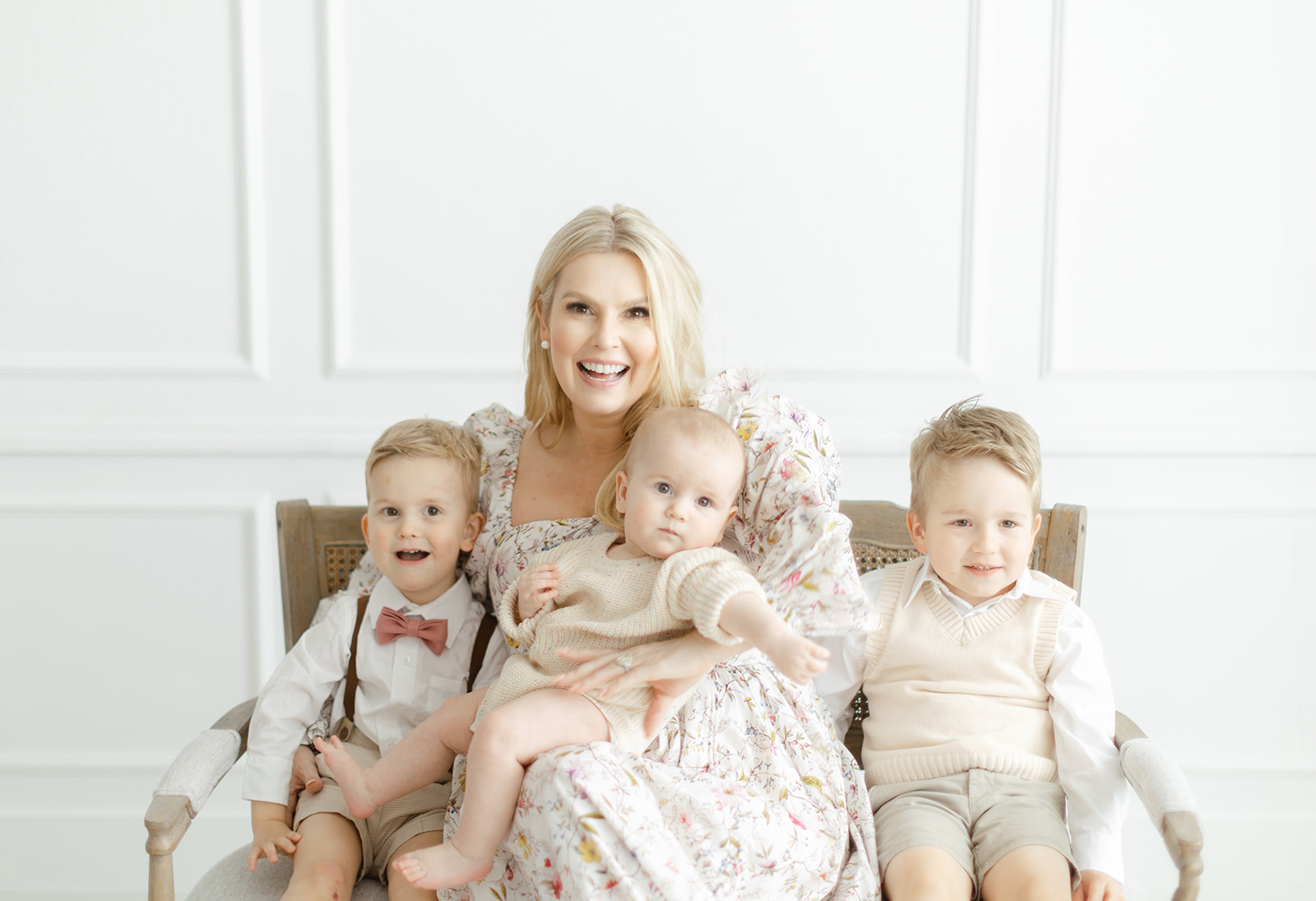 A happy mother sits on a wooden bench in a studio with her three toddler sons before meeting with Dallas Nannies