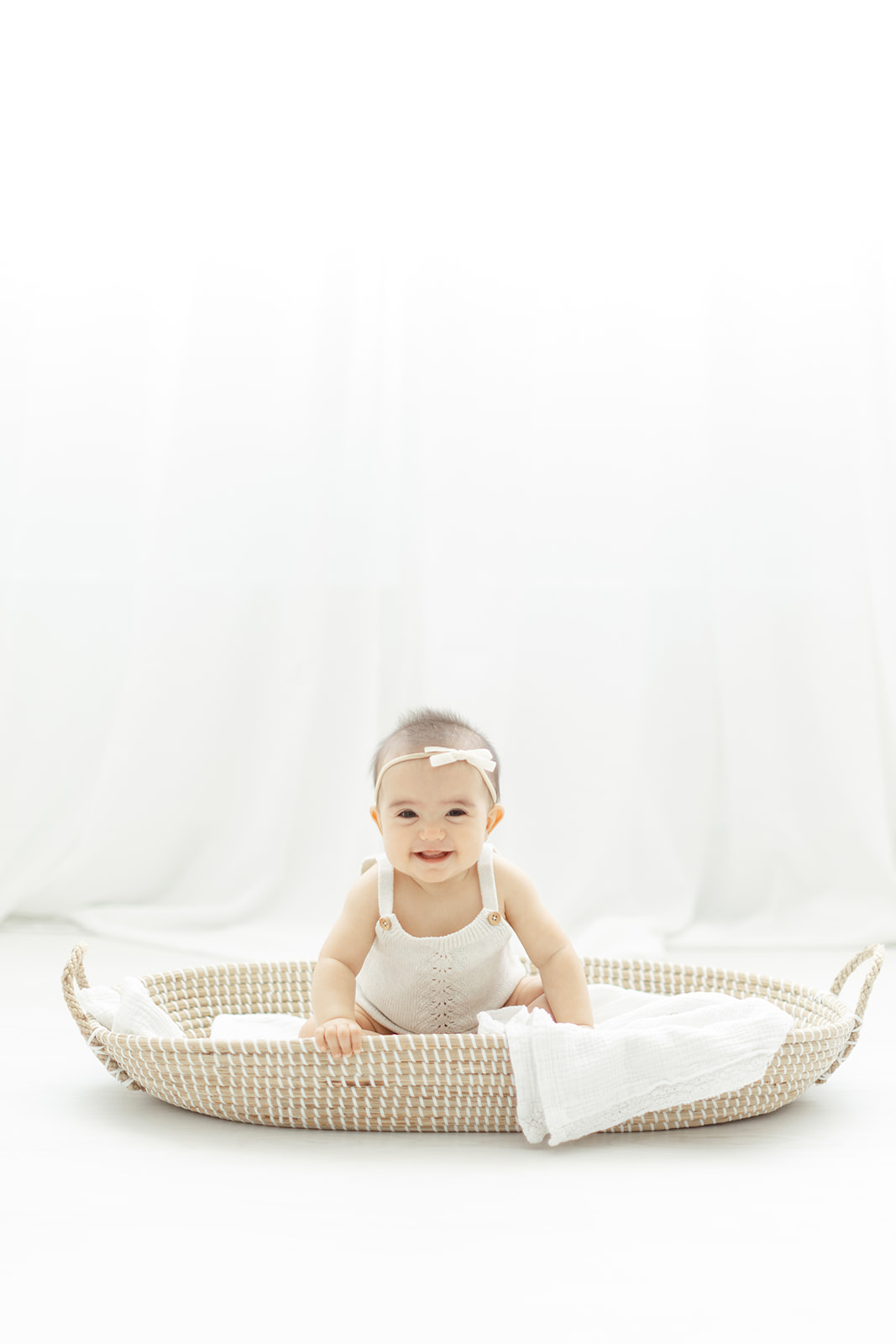 A toddler girl plays in a shallow woven basket under a window in a studio