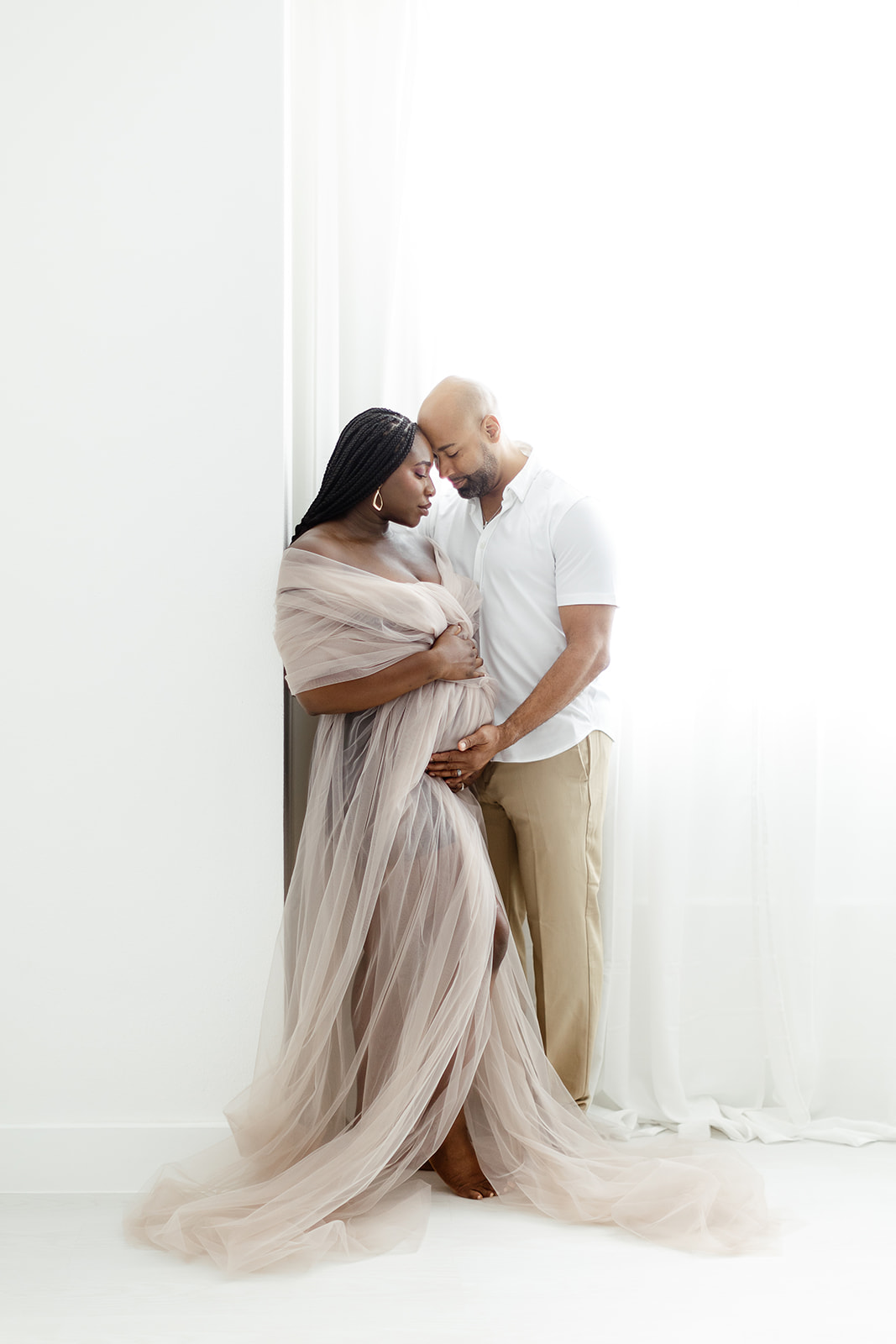 Expecting parents share an intimate moment touching foreheads and holding the bump in a studio window
