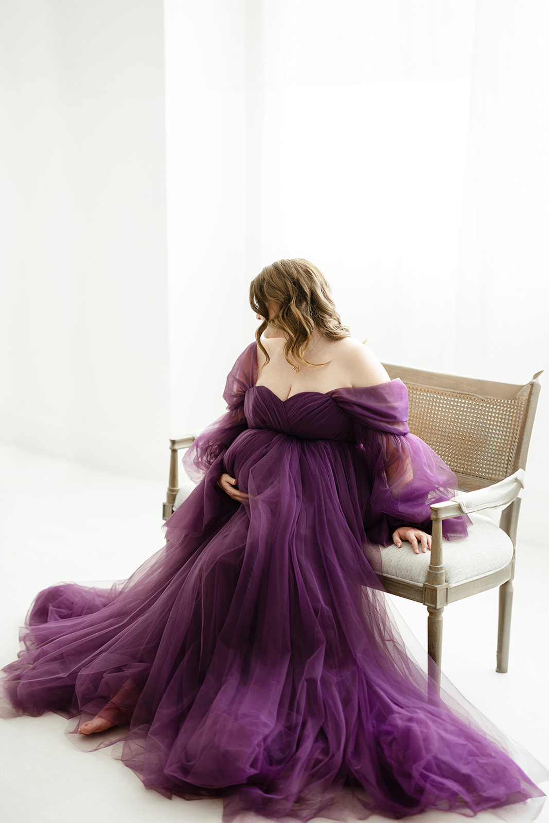 A mother to be in a purple tule maternity gown sits on a bench before visiting a Prenatal Chiropractor Dallas